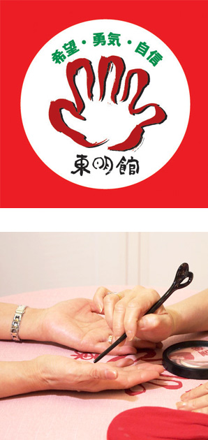 写真の上段:東明館のロゴマーク/下段:黒い指し棒を使って両手の手相占いの鑑定中